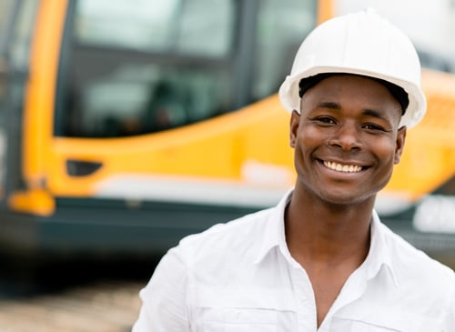 Construction worker with machines at the background looking happy